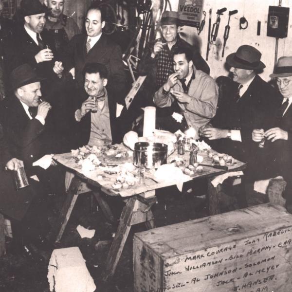A group of Sephardic men socialize while eating seafood inside the garage of Pacific Fish & Oyster Co. (1940-45)