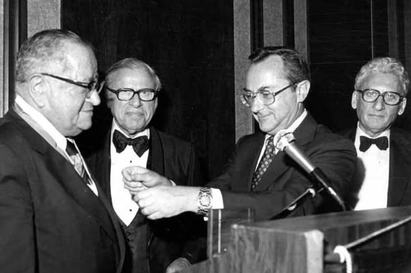 Morris Polack and Sol Esfeld with two other men behind podium at event, approximately 1983