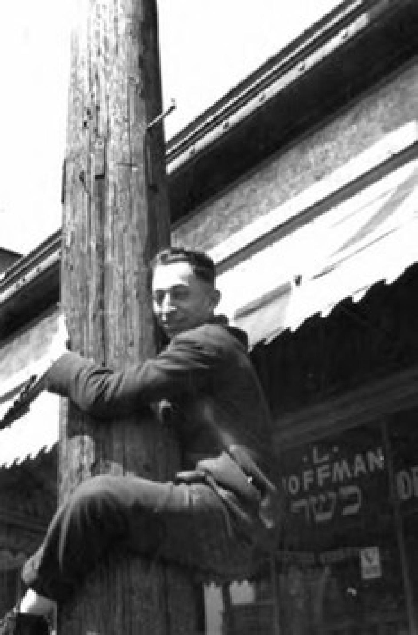 Abe Hoffman climbing telephone pole in front of Hoffman Kosher Deli and Grocery at 1714 Yesler Way, Seattle, ca. 1920s-1930s