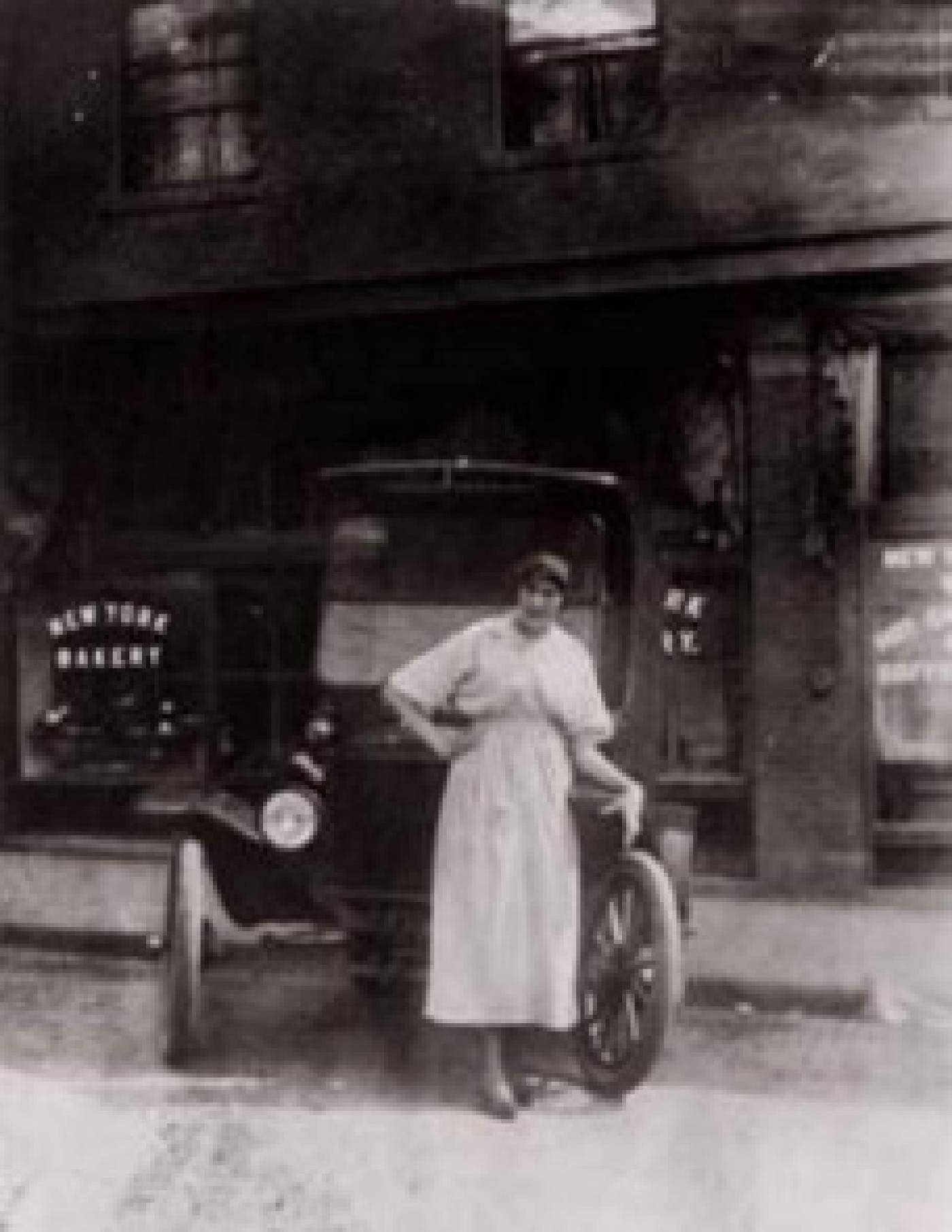 Hazel Levine leaning against car in front of New York Bakery, 661 Weller St., Seattle, ca. 1910