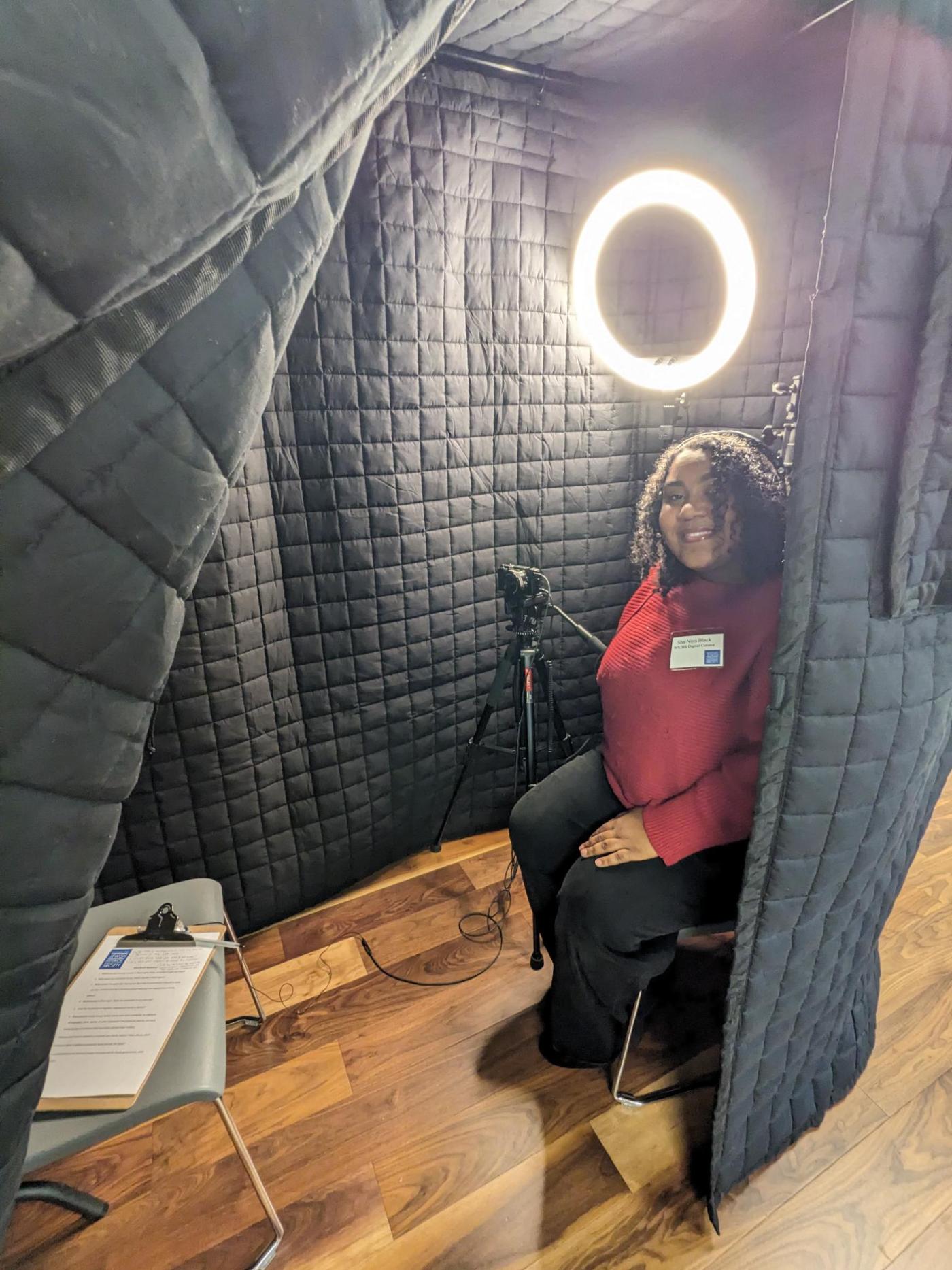 Digital curator, Sha'Niya Black sitting in the Storybooth