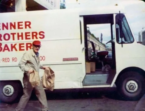 Charlie Brenner in front of a Brenner Brothers delivery truck Charlie holding bags full of goodies in front of a Brenner Brothers delivery truck in Bellevue, ca. 1970-1975